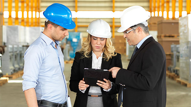 three business people wearing hard hats looking at tablet device