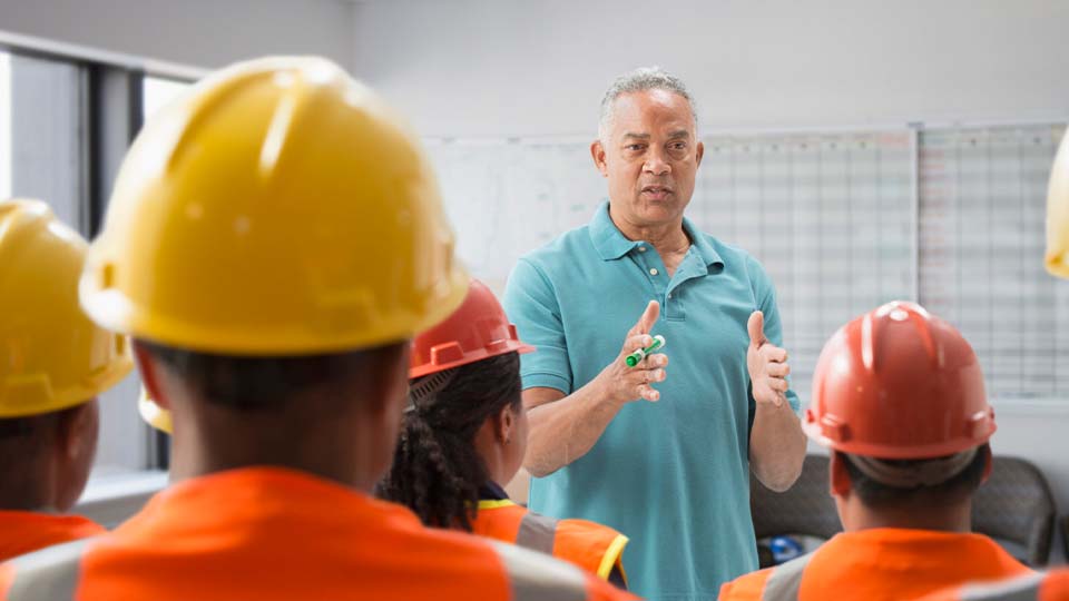 Man presenting to a group of people wearing safety hats