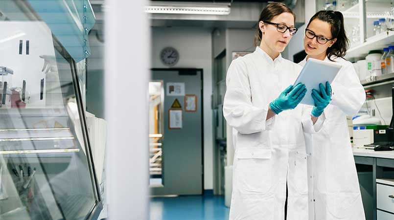 two female laboratory scientists discussing data on a tablet device