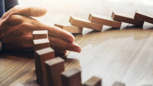 Hand stopping the domino effect with wooden blocks