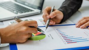 hands holding pens that are pointed towards a point on a pie chart graph
