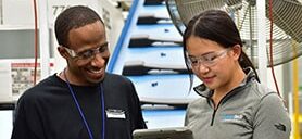 Man and woman wearing safety glasses discussing ergonomics data via tablet
