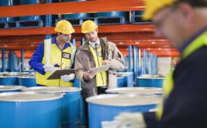 Workers reading clipboards and looking at tablet device in chemical warehouse