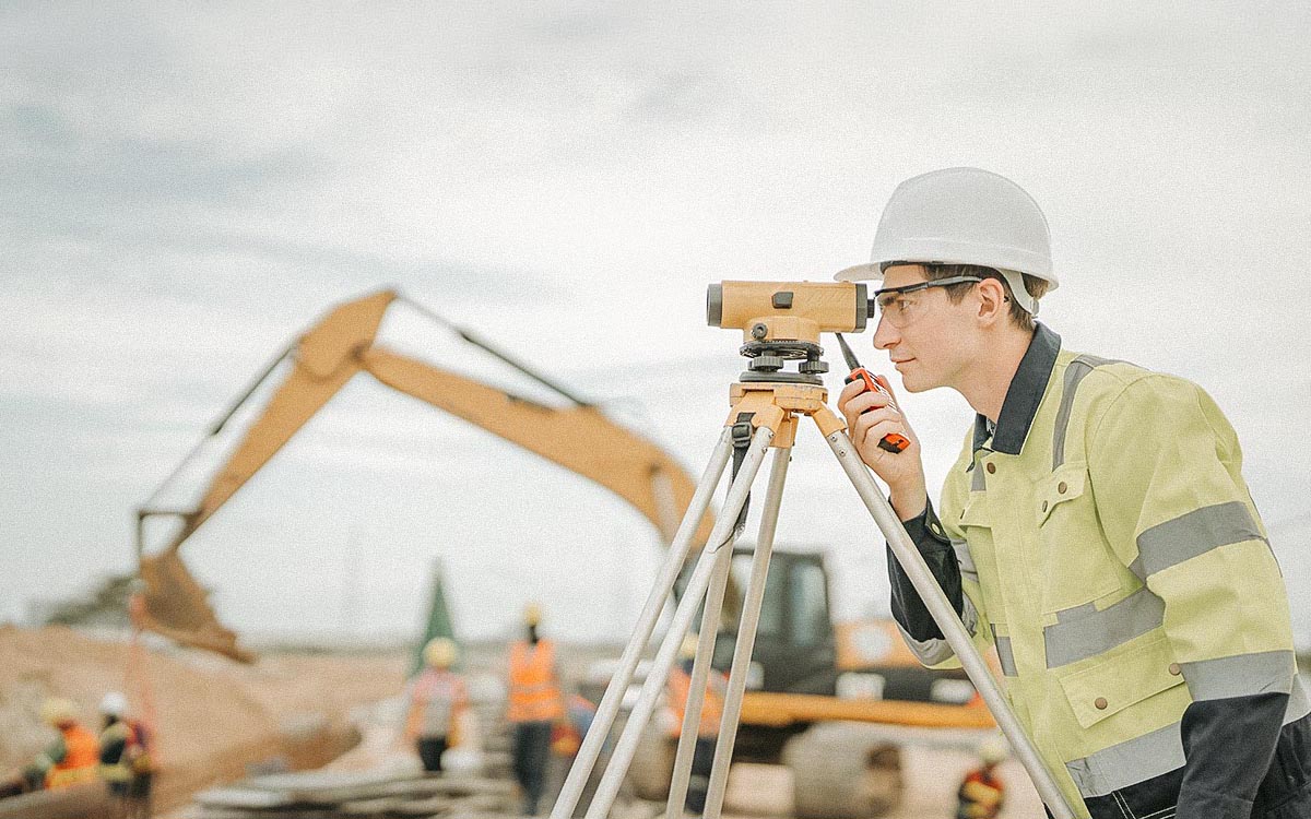 Male Engineer Working With Survey Equipment On Construction Site And Worker Background