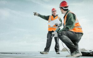 Building Foreman Holding Plans And Directing Apprentice On Factory Roof
