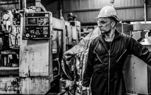 Portrait Handsome Worker With Safety Suit And Old Machine In Factory.
