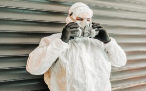 A Man Wearing Ppe, Goggles, Surgical Mask And Active Carbon Protective Mask To Protect Himself From Covid 19 On Industrial Background