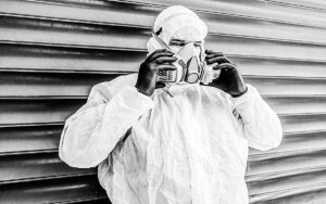 A Man Wearing Ppe, Goggles, Surgical Mask And Active Carbon Protective Mask To Protect Himself From Covid 19 On Industrial Background
