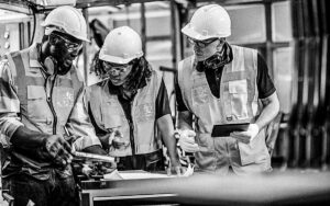 Reduce Manufacturing Waste Solution. Group Of Manufacturing Process Engineers Having A Discussion About Welding Assembly Process Improvement To Reduce Parts Defect During Production In Front Of The Production Line.