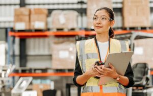 Portrait Of Female Warehouse Supervisor Working In Leading Distribution Warehouse. She Having Skilled In Audit Daily Operations, While Controlling And Managing Inventory And Logistics.