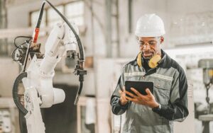 African American Engineer Working Automatic Robotic Arm Machine In Factory. Male Technician Worker Maintenance Automatic Robotic Hand In Smart Factory, Industrial And Manufacturing Concept.